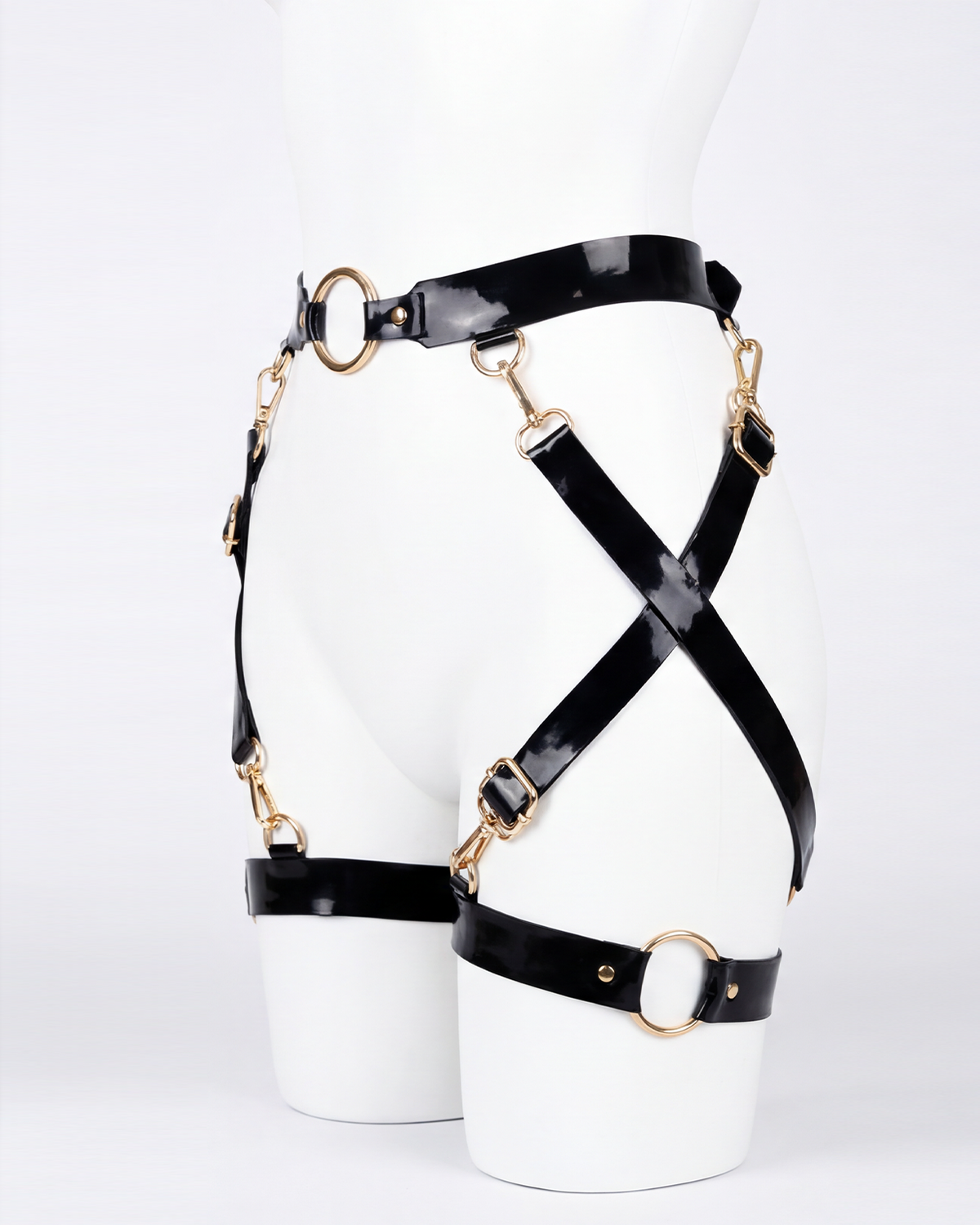 A glossy black latex waist and leg harness set by Ribcage, featuring structural straps, metallic O-rings, and adjustable buckles.