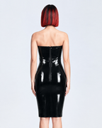 A model shown in profile wearing a glossy black latex strapless dress by Ribcage, highlighting the corset-style waist, the form-fitting pencil silhouette, and the compressive second-skin fit.