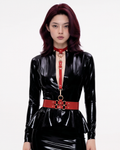A model shown from the front wearing The Aurora Harness Set in red latex over a black latex dress, featuring a buckled choker, vertical chest strap, and a structured waist belt, accented with gold metallic O-rings and hardware.