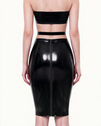A model shown from the back wearing a high-shine black latex high-waisted pencil skirt by Ribcage, featuring a contrasting waistline design and a full-length back zipper closure, styled with a matching strapless bandeau top.