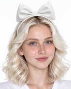A model shown from the front wearing a high-shine white latex headband by Ribcage, featuring a sleek band crowned with a dramatic, oversized structural bow at the top.