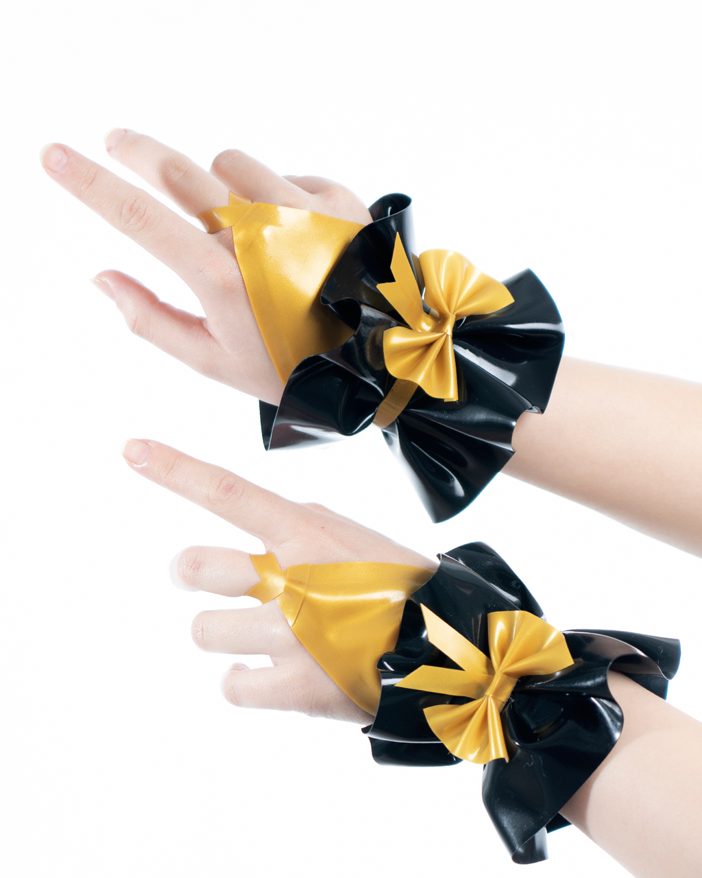 A model shown wearing a pair of high-shine metallic gold and black latex hand cuffs by Ribcage, featuring a flared ruffled cuff design, a contrasting black bow, and an integrated finger loop.