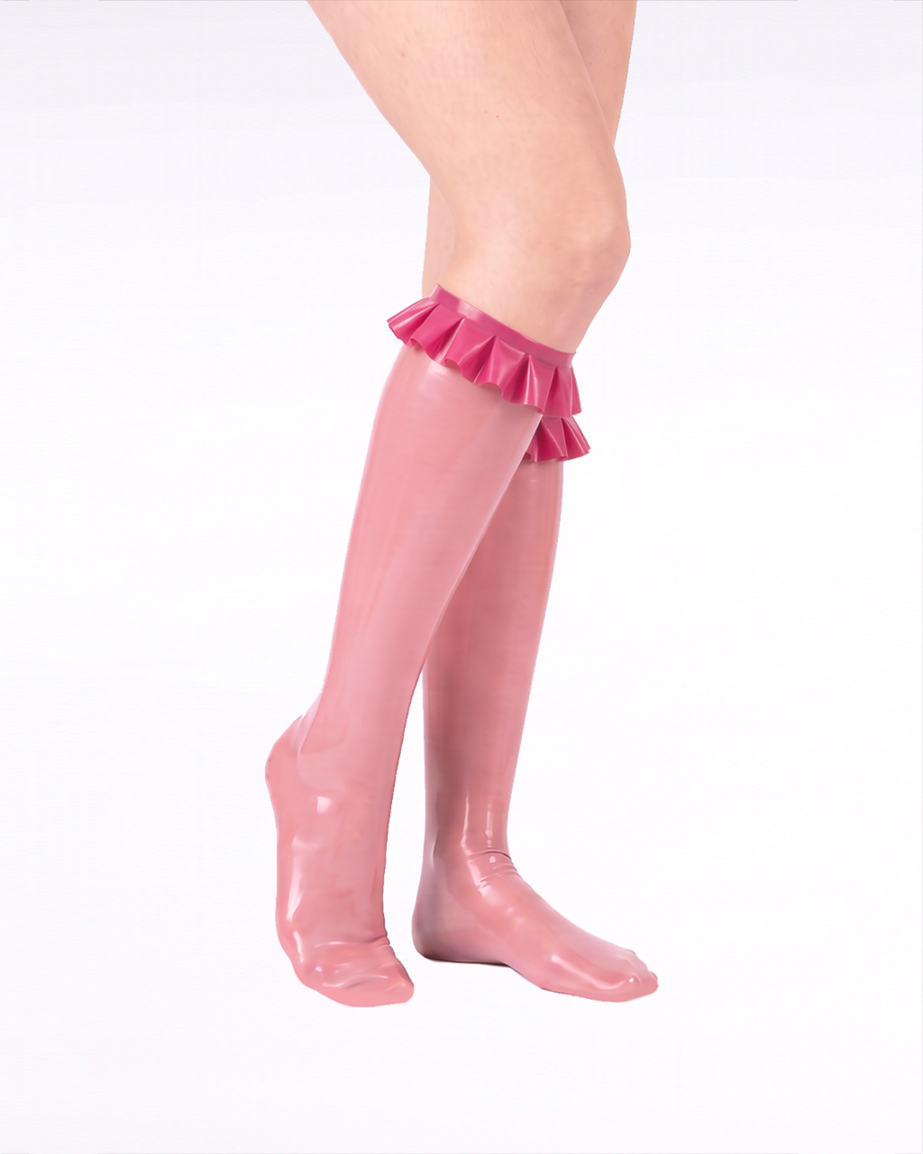A side view of a model's legs wearing high-shine metallic pink latex knee-high socks by Ribcage, highlighting the sleek silhouette and contrasting vivid fuchsia ruffled trims at the cuffs.