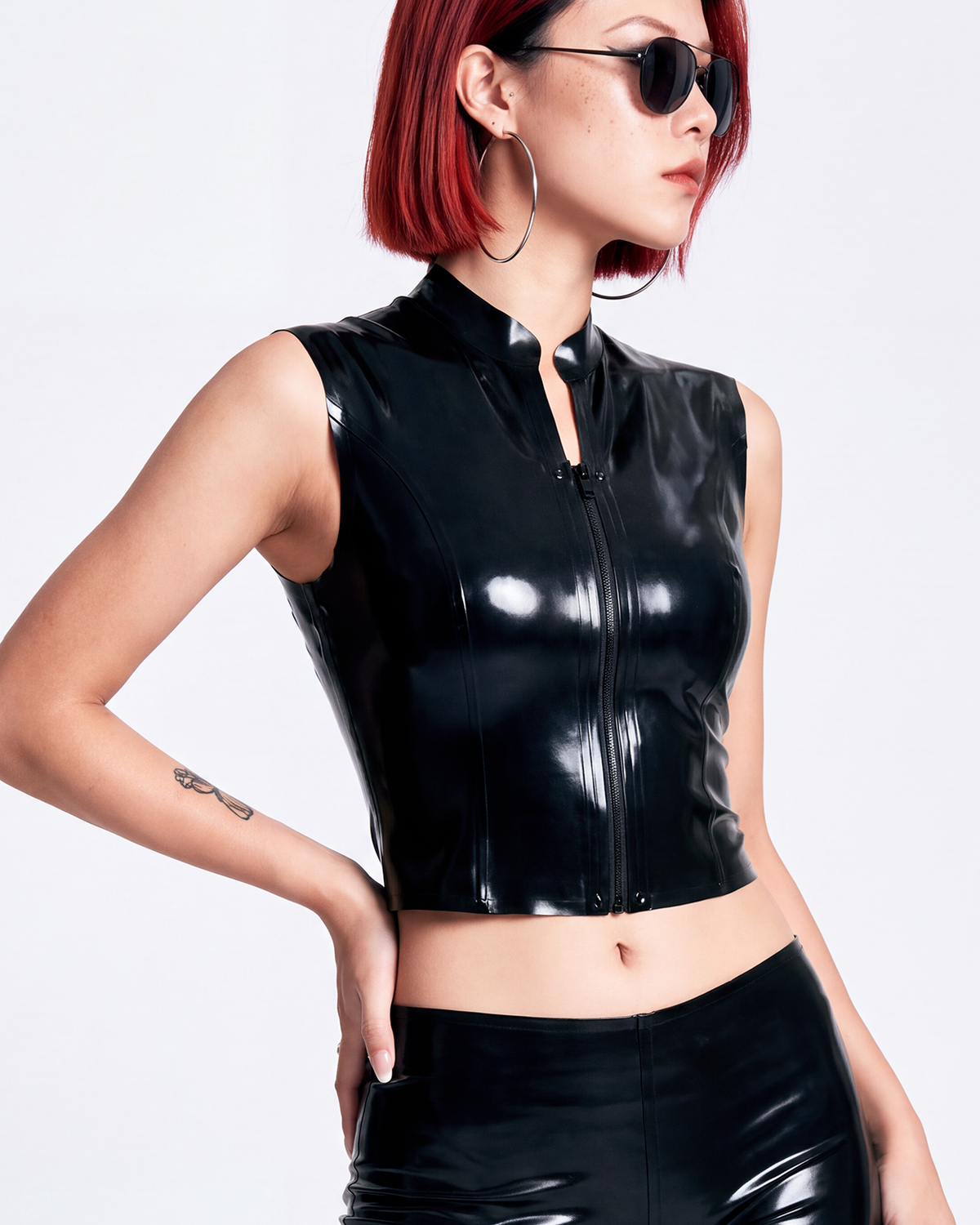 A model shown in profile wearing a high-shine black latex sleeveless top by Ribcage, highlighting the structured mock neck, the bold front-zip closure secured with snap buttons, and the compressive second-skin cropped silhouette.