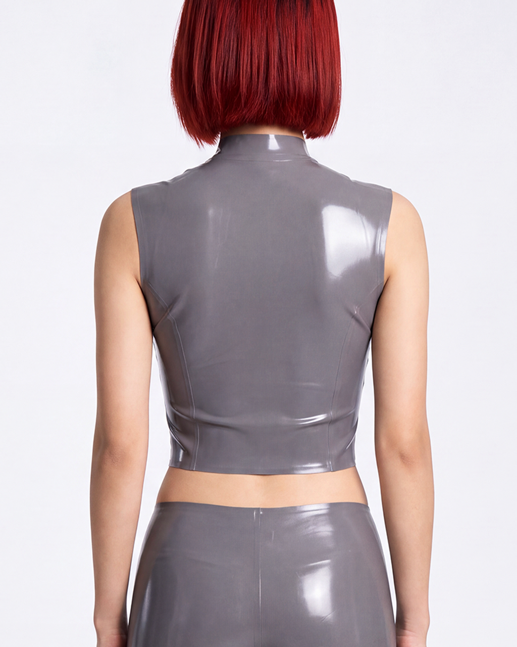 A model shown from the back wearing a high-shine metallic taupe-grey latex sleeveless top by Ribcage, featuring a structured mock neck and a compressive second-skin cropped silhouette.