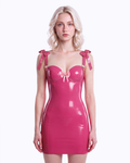 A model shown from the front wearing a high-shine vivid fuchsia latex bodycon slip dress by Ribcage, featuring a sweetheart neckline with structural piping, a metallic pink center bow, and matching metallic pink structural bows on the shoulder straps.