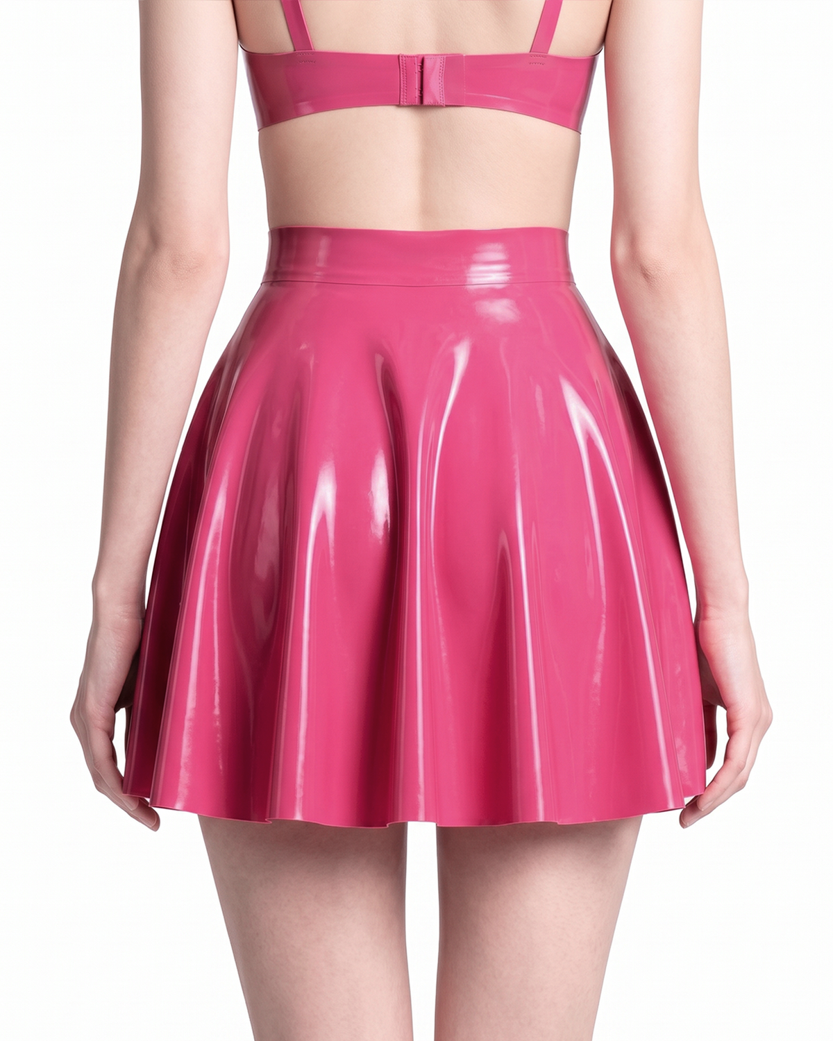 A model shown from the back wearing a high-shine vivid fuchsia latex short skirt by Ribcage, highlighting the seamless flared A-line silhouette and voluminous drape, styled with a matching crop top.