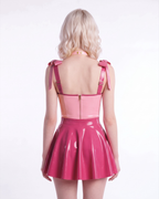 A model shown from the back wearing a high-shine two-tone pink latex three-piece ensemble by Ribcage, highlighting the metallic pink Fondant Bodysuit, the vivid fuchsia high-waisted Fondant Skirt, and the matching metallic pink Eloise Bow Choker.