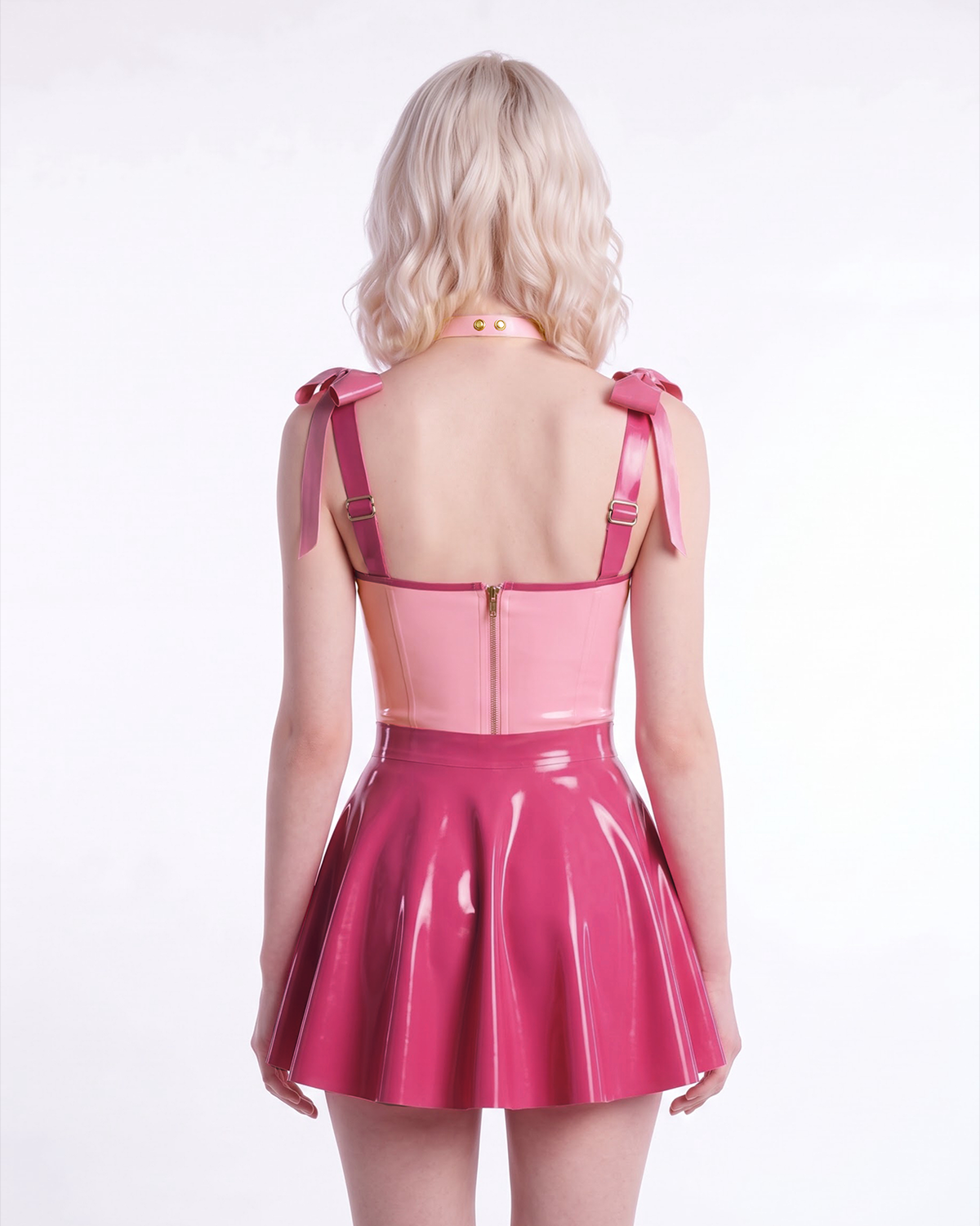 A model shown from the back wearing a high-shine two-tone pink latex three-piece ensemble by Ribcage, highlighting the metallic pink Fondant Bodysuit, the vivid fuchsia high-waisted Fondant Skirt, and the matching metallic pink Eloise Bow Choker.