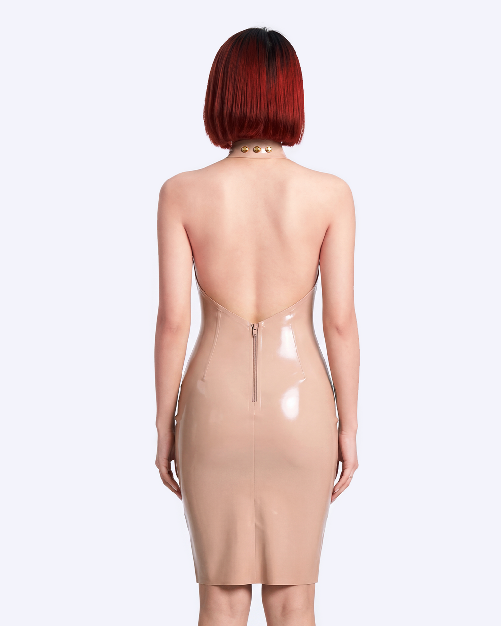 A model shown from the back wearing a high-shine nude latex mock-neck dress by Ribcage, featuring a dramatic deep open back, a matching choker-style collar with gold studs, and a compressive second-skin pencil silhouette.
