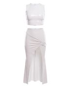 A high-shine white latex two-piece ensemble by Ribcage, featuring a minimalist sleeveless crop top and a high-waisted maxi skirt with a dramatic side slit and a polished metal buckle accent, designed with a compressive second-skin fit.