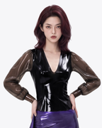 A model shown from the front wearing the high-shine black latex Ripple Blouse by Ribcage, highlighting the deep V-neckline and semi-transparent smoky balloon sleeves.
