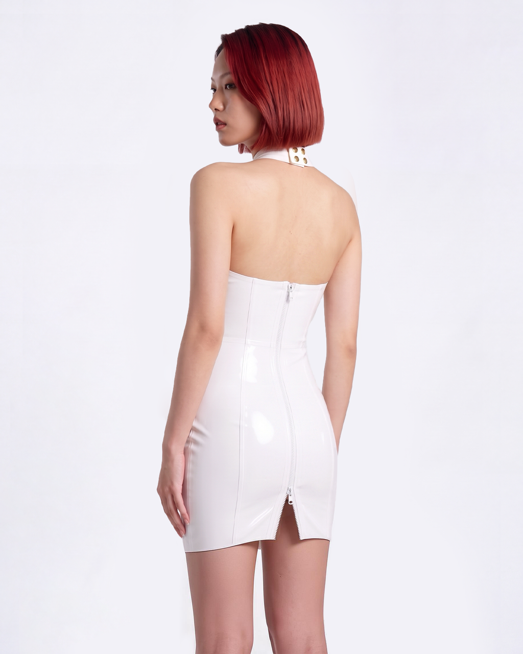 A model shown from the back wearing a high-shine white latex halter-neck dress by Ribcage, featuring an open back design, a high-neck collar, a prominent central zipper, and a compressive second-skin pencil silhouette.