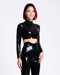 A model shown in profile wearing a high-shine metallic black latex long-sleeve crop top by Ribcage, highlighting the structured mock neckline, the sharp cropped hemline, and the compressive second-skin fit.