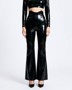 A model shown from the front wearing a pair of glossy metallic black latex high-waisted flared trousers by Ribcage, featuring a sharp architectural drape, distinctive side button details, and a compressive second-skin fit.