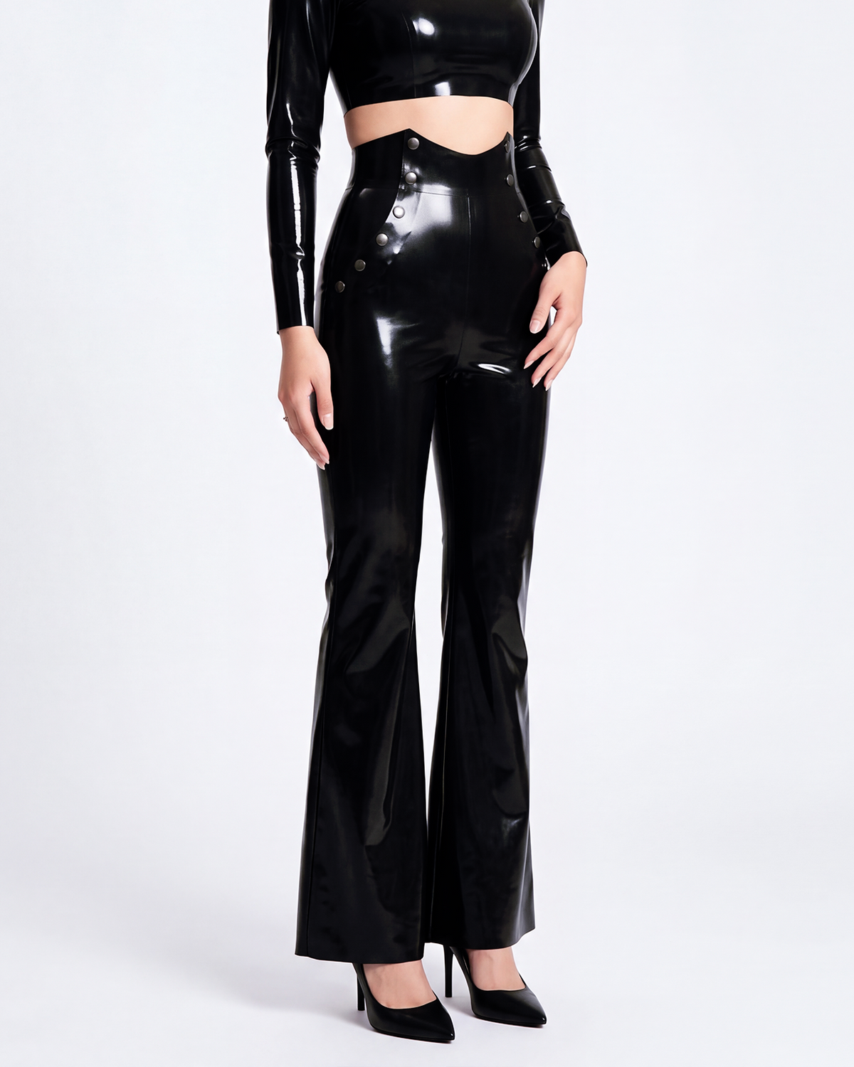 A model shown in profile wearing a pair of glossy metallic black latex high-waisted flared trousers by Ribcage, highlighting the sharp architectural drape, the distinctive side button details, and the compressive second-skin fit.