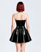 A model shown from the back wearing a high-shine black latex strapless cocktail dress by Ribcage, featuring a corset-style bodice, a flared A-line skirt, a compressive second-skin fit, and a matching minimalist choker.